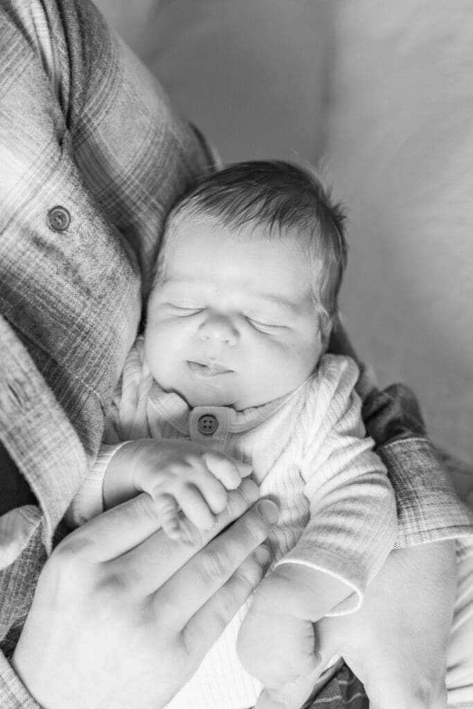 Black and white photo of newborn resting in dad's arms at in-home session