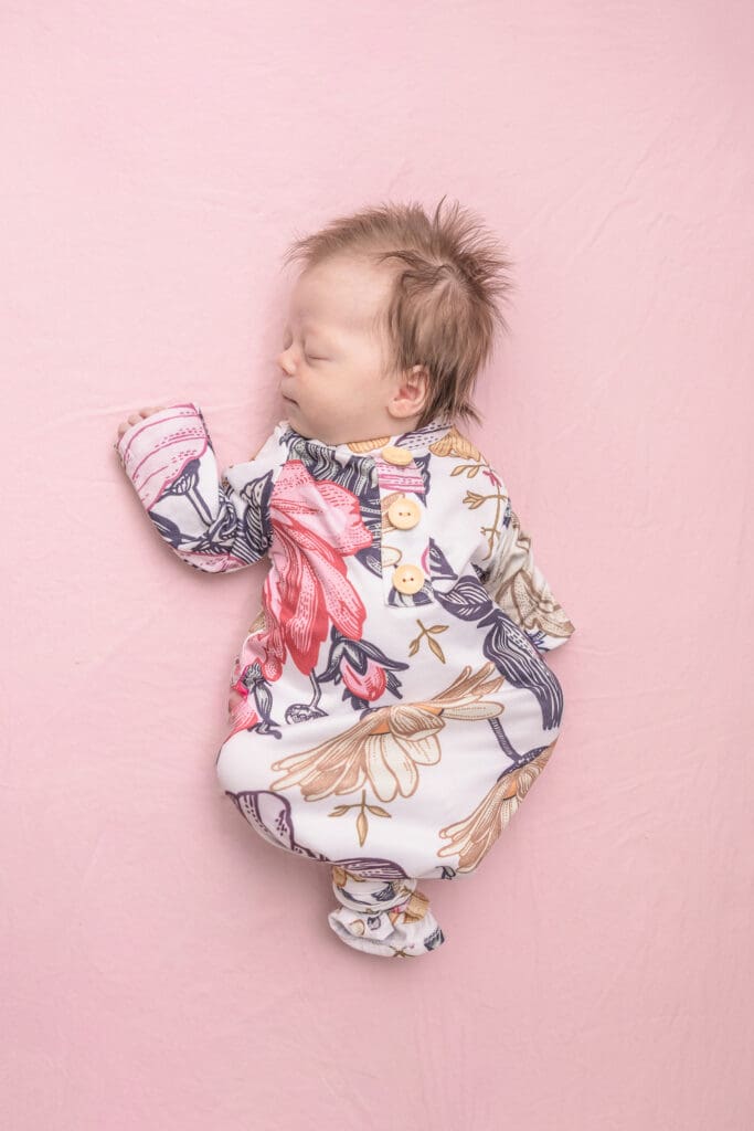 Sleeping newborn in floral outfit on soft pink blanket