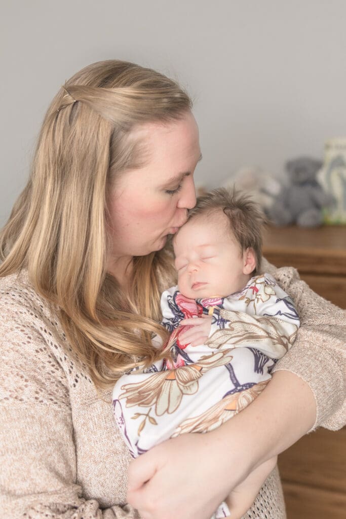 Mom gently kissing her sleeping newborn during in-home session