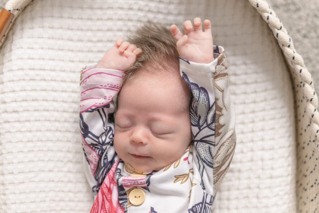 Newborn baby stretching arms while sleeping in woven basket