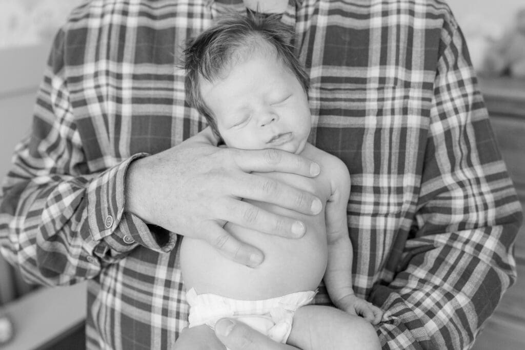 Dad holding newborn upright while baby sleeps in his hands