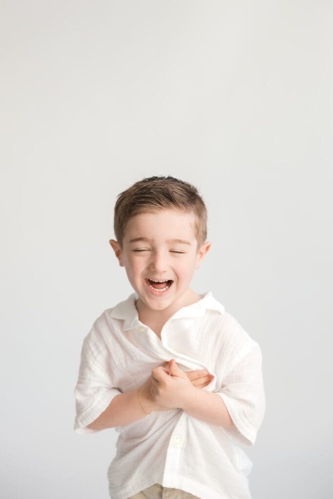 Young boy laughing in white shirt during bright child portrait session