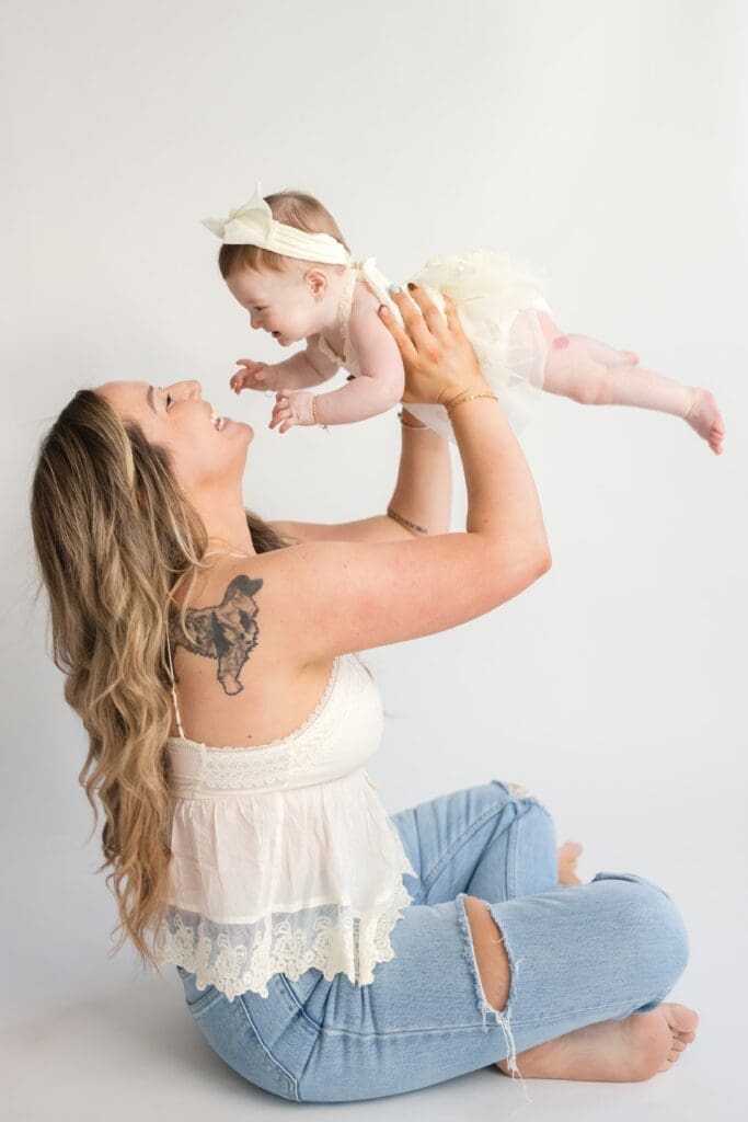 Mom holding baby girl up while smiling during family portrait session
