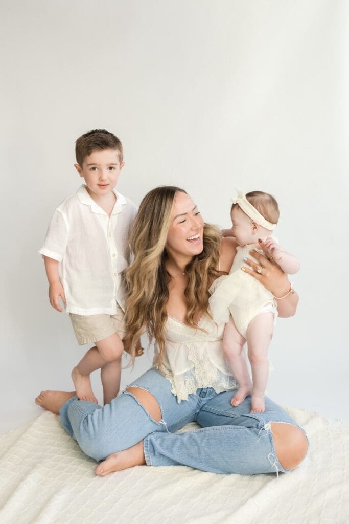 Mom smiling at baby girl while young son stands beside her in studio