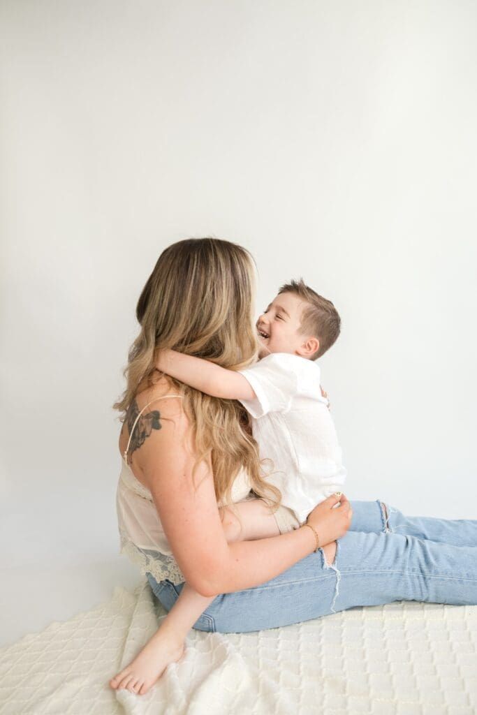 Young boy hugging his mother while laughing during studio family portraits