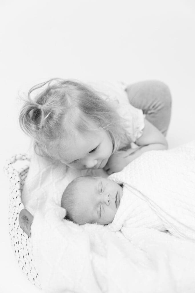 Older sibling leaning close to newborn baby during studio newborn session