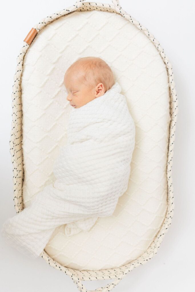 Newborn baby sleeping peacefully in a white swaddle during studio session