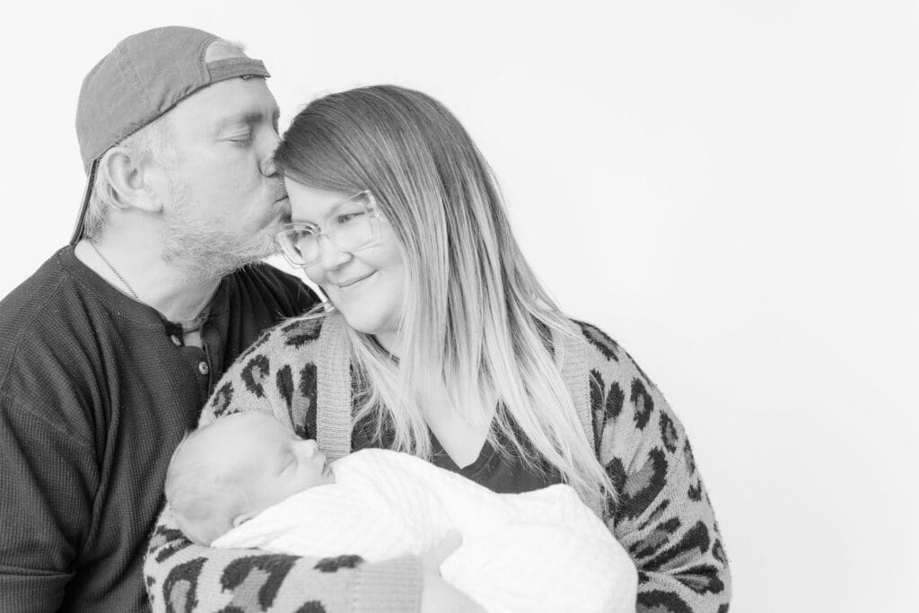 New parents cuddling sleeping newborn during black and white family portrait