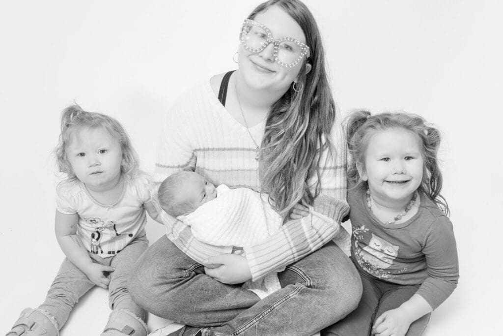 Older sisters sitting together while holding newborn during family portrait
