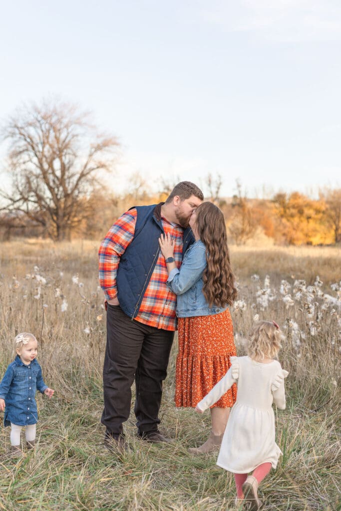 Candid family photo with parents embracing and children playing outdoors