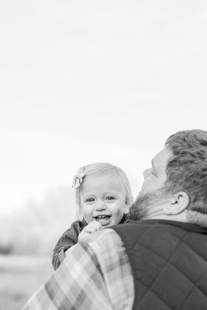 Happy toddler laughing over her father's shoulder during an outdoor family session