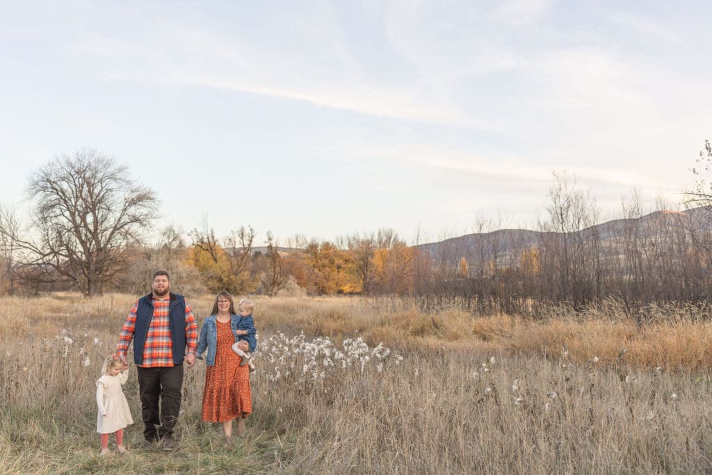 Parents and daughters walking hand in hand through a grassy field during golden hour