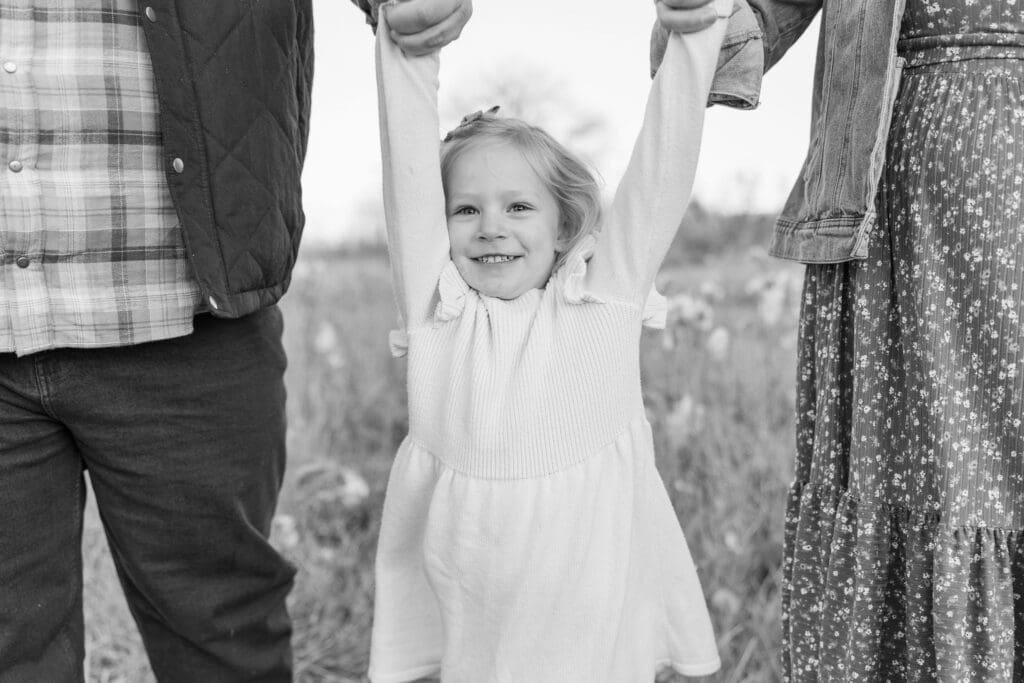 Playful family photo featuring a young girl swinging between her parents