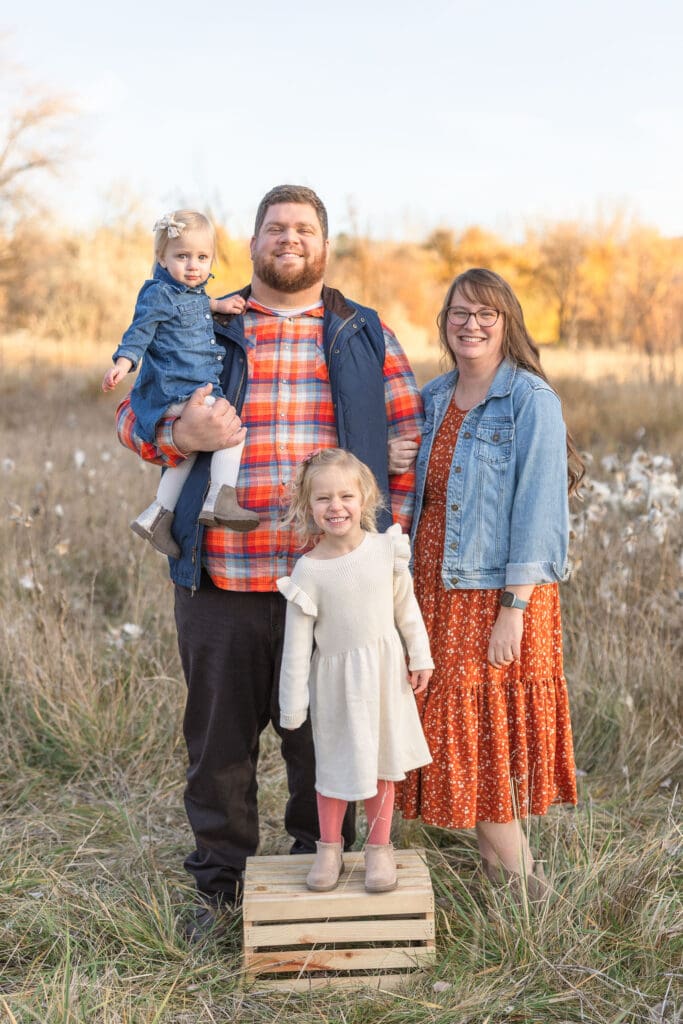 Family of four posing together in a golden field during an outdoor fall family photo session